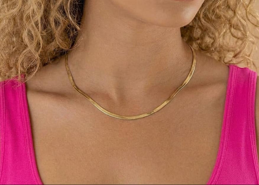 Woman wearing a gold herringbone necklace with a pink top against a beige background