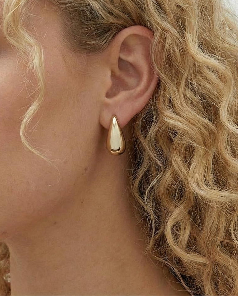 Close-up of a person wearing a gold teardrop earring with blonde hair.