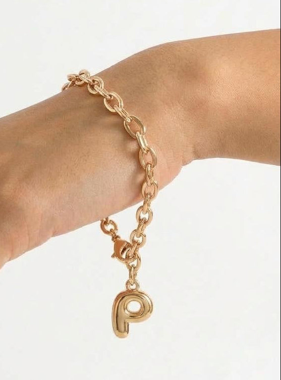 Gold chain bracelet with a letter charm on a wrist against a white background