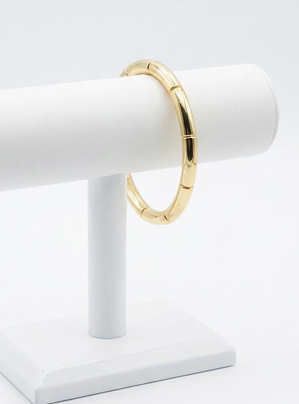 Gold bracelet on a white jewelry stand against a light gray background