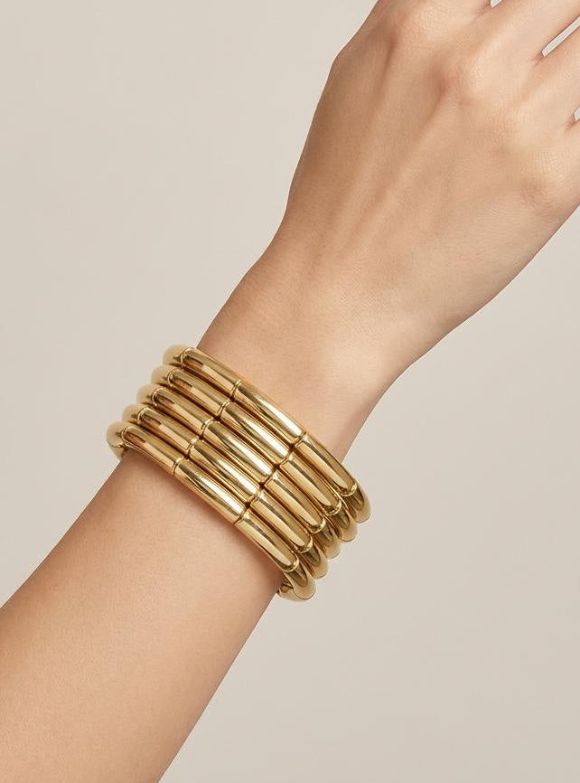 Hand wearing multiple gold bracelets on a neutral background
