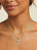 Woman wearing a gold necklace with an eye pendant on a beige background
