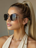 Gold-tone minimalist glasses chain with elongated links and clear silicone eyewear loops, displayed on a model 