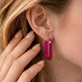 Close-up of a person wearing bright pink earrings with a hand adjusting hair.