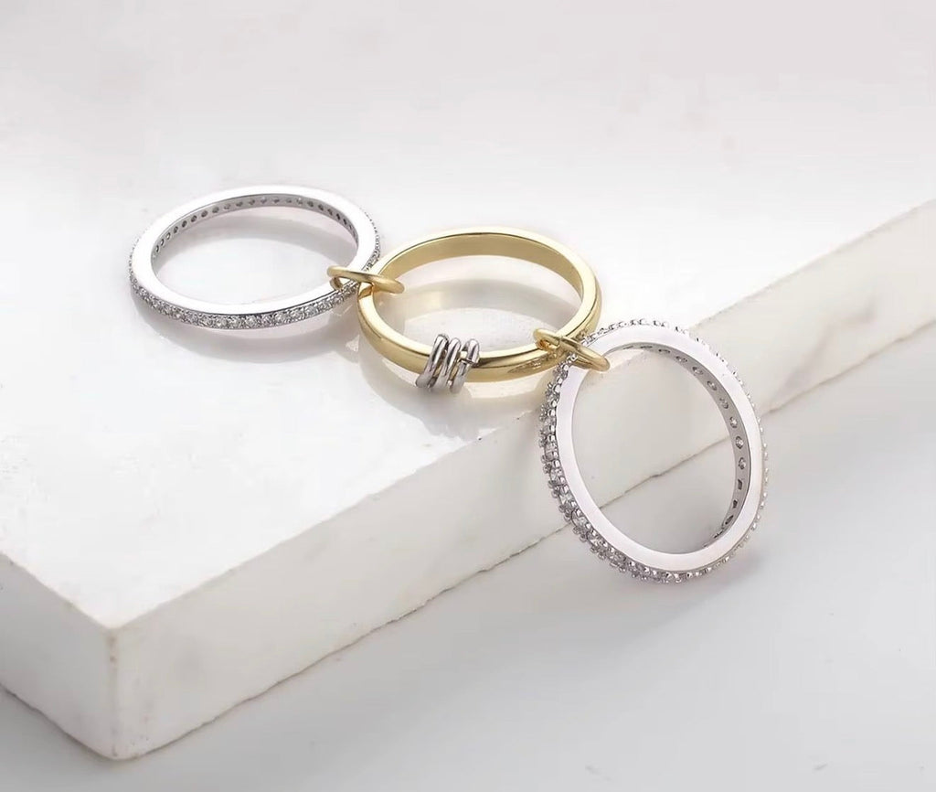 Three rings in silver, gold, and white on a light gray surface