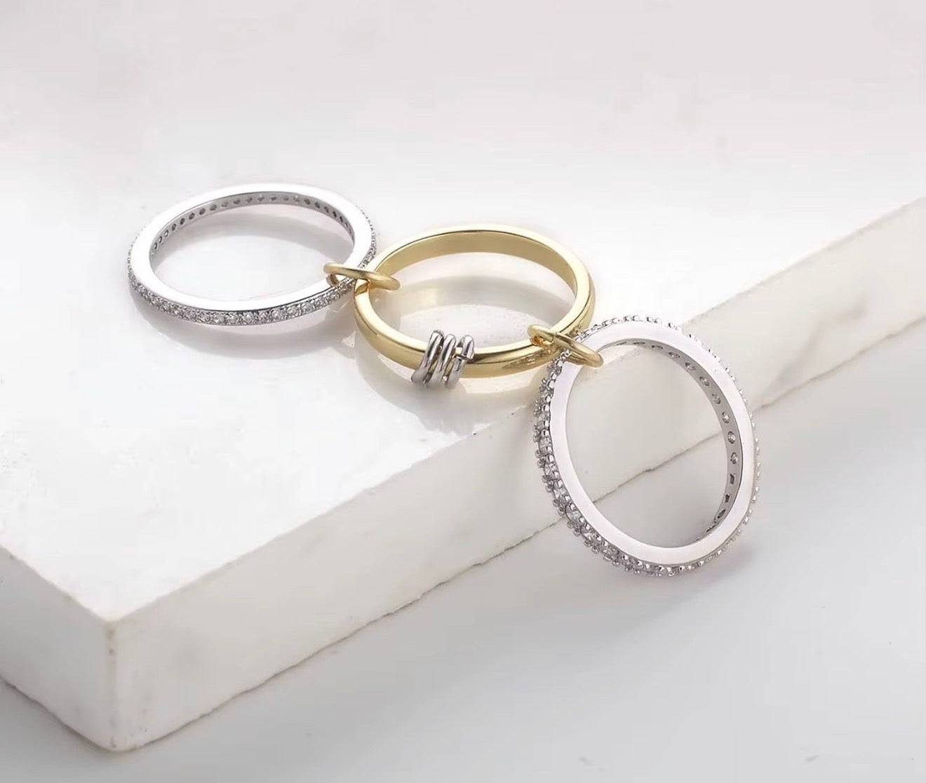 Three rings in silver, gold, and white on a light gray surface