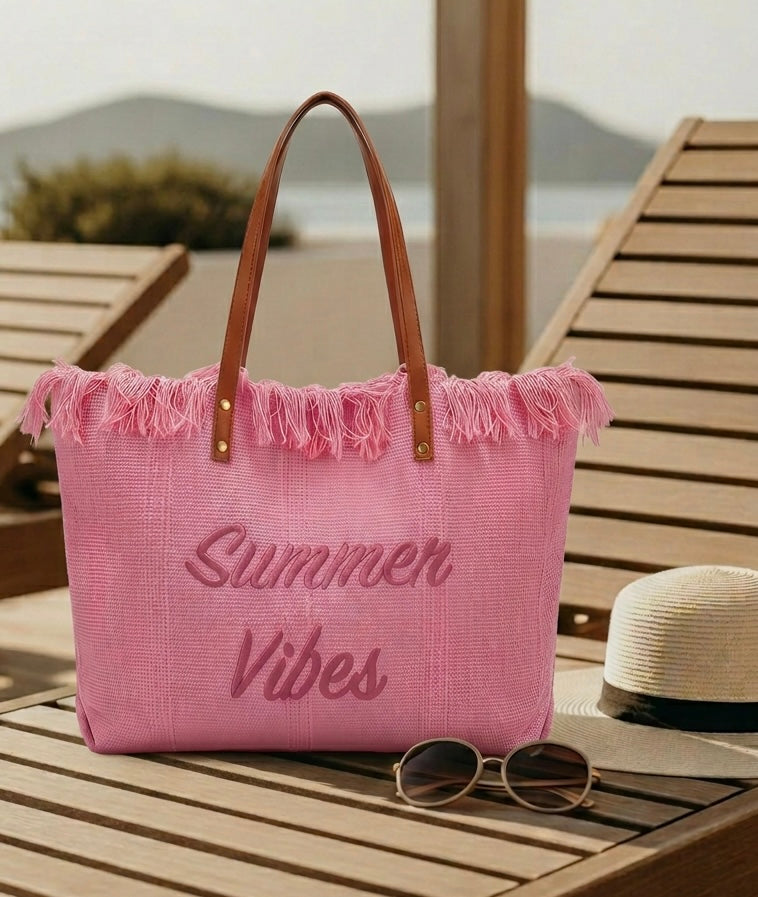 Pink tote bag with 'Summer Vibes' text on a wooden surface by the beach.