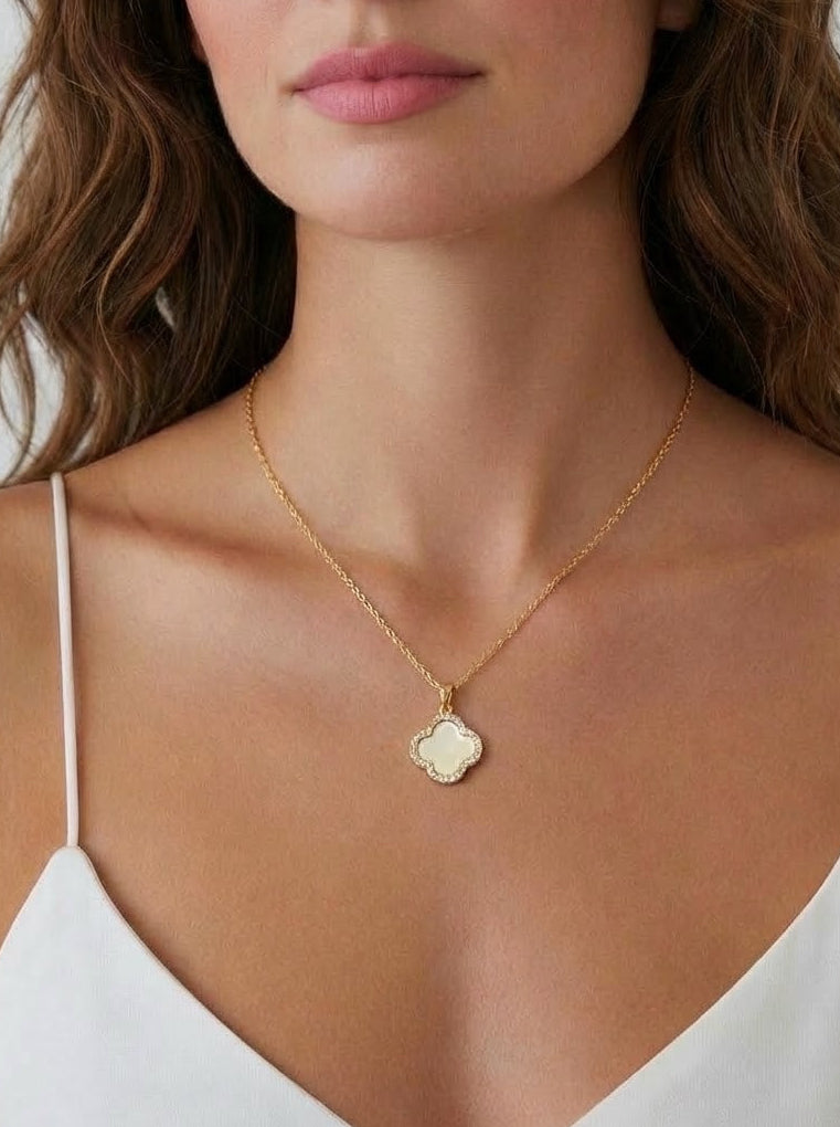 Woman wearing a gold clover mother of pearl necklace with a pendant against a neutral background
