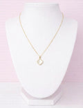 Gold clover necklace with a heart pendant on a white stand against a pink gradient background