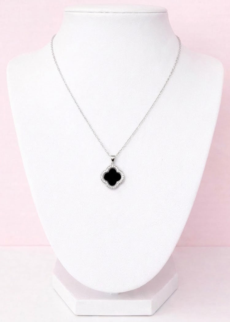 Silver Clover Necklace with a black pendant on a white stand against a pink background
