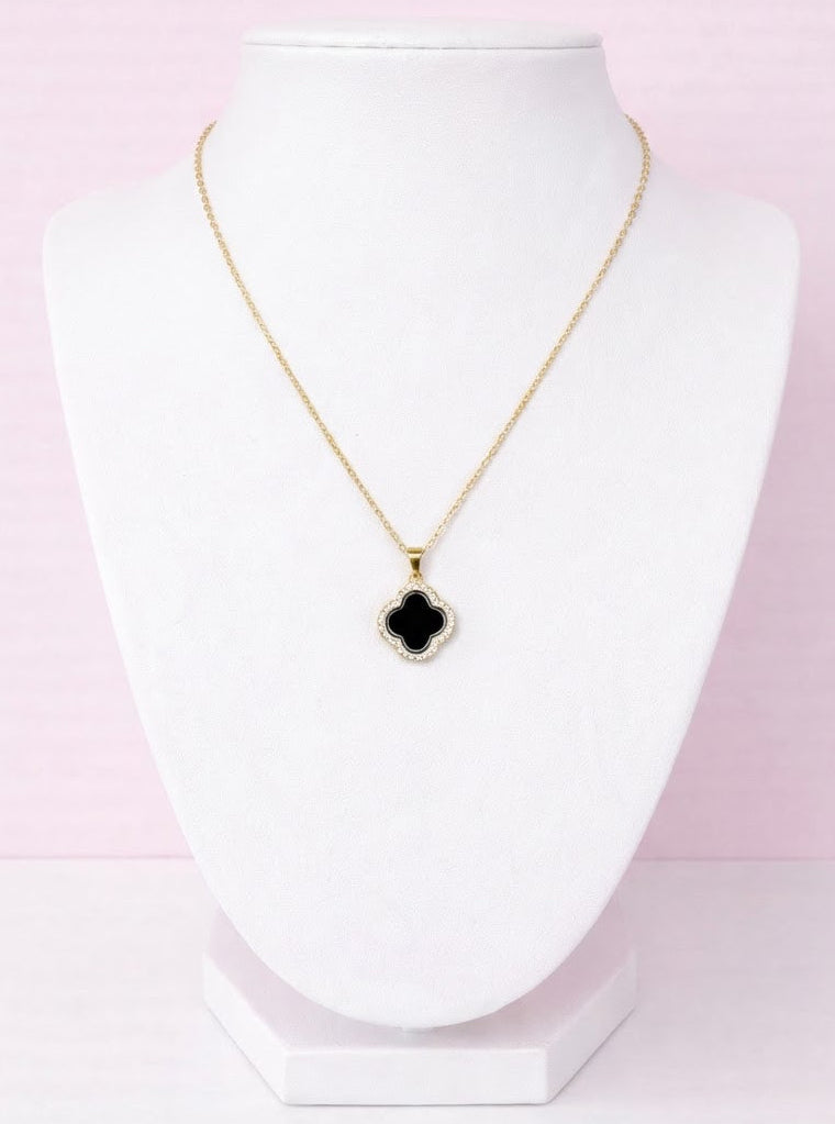 Clover Necklace with a black pendant on a white stand against a pink background