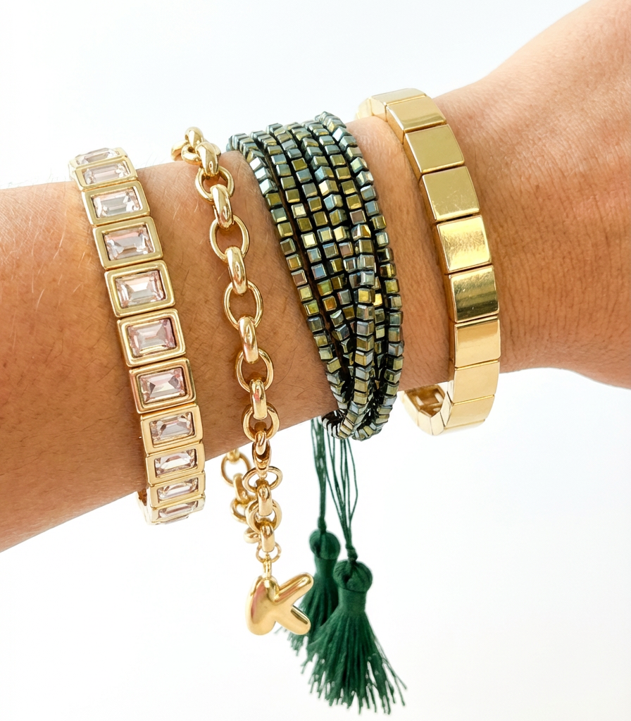 Hand wearing multiple gold and green bracelets stacked on a white background