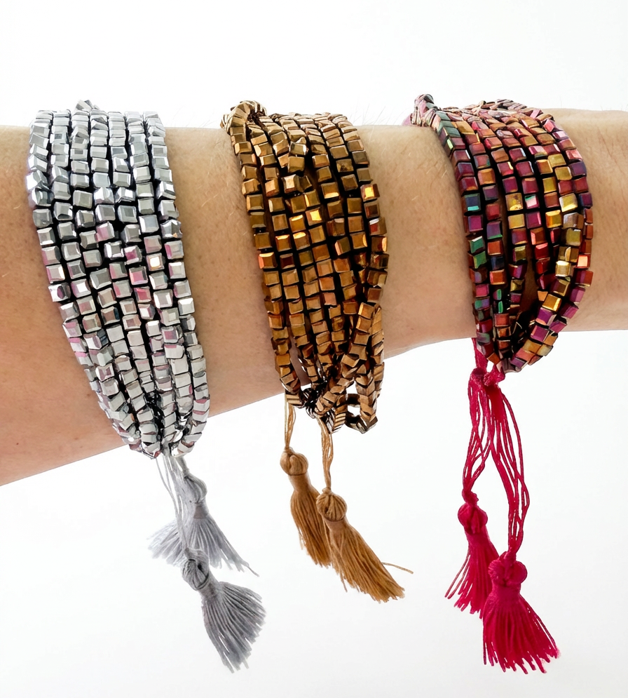 Three beaded bracelets with tassels on a wrist against a white background