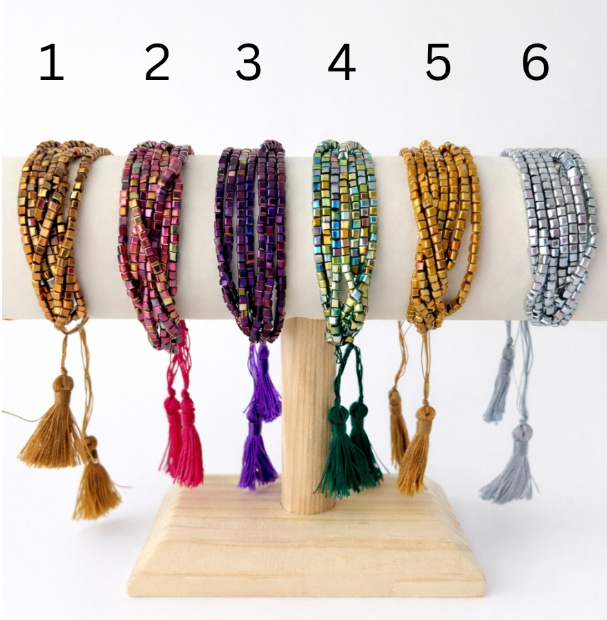 Set of six beaded bracelets with tassels on a wooden stand against a white background.